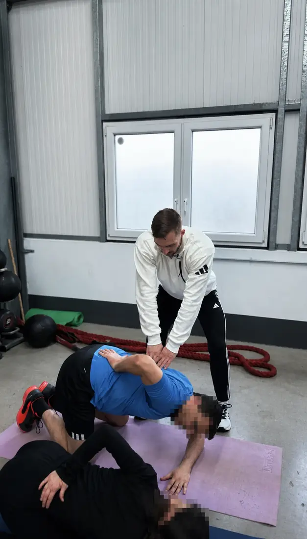 Lukas Leo Plasil begleitet zwei anonymisierte Teilnehmende bei einer Bewegungsaufgabe am Boden